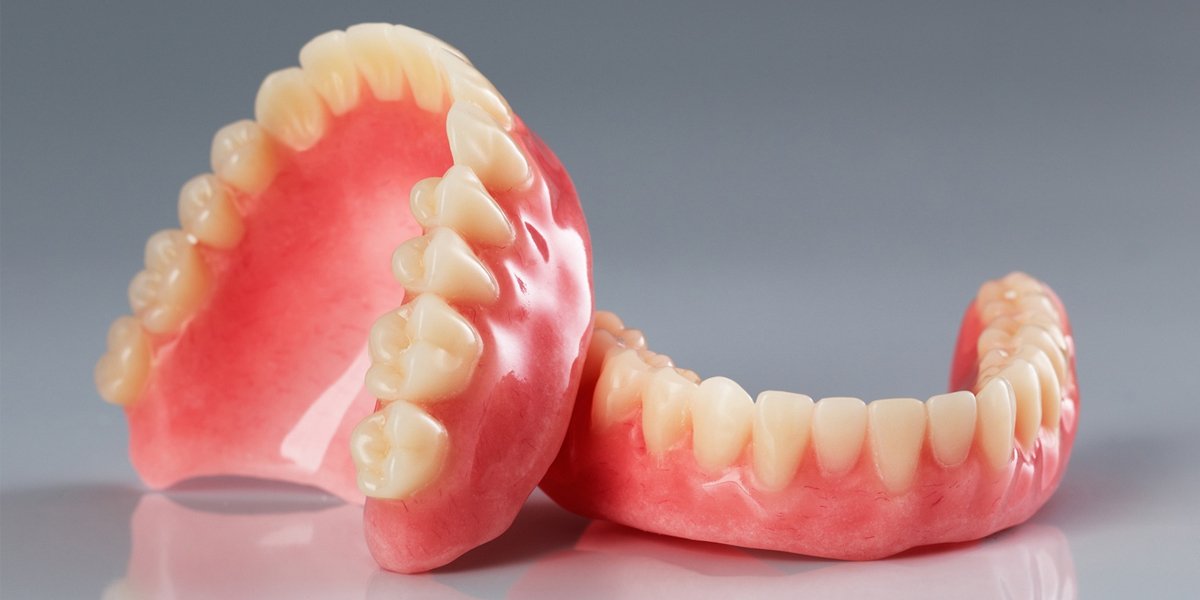 A set of upper and lower full dentures on a gray background.