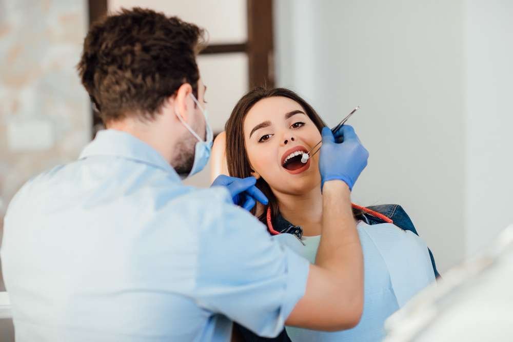 A dentist examining a smiling woman’s teeth during a dental checkup.