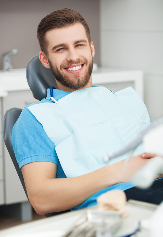 A man smiling while sitting in a dental chair with a bib on.