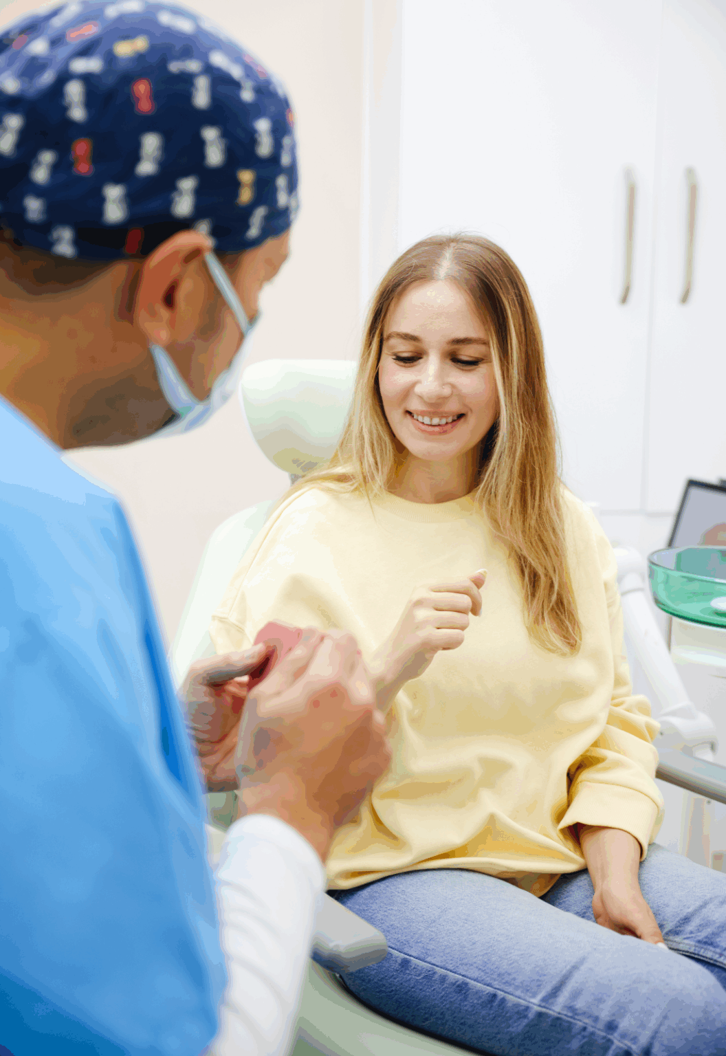 A dentist in blue scrubs explains a dental model to a smiling female patient during a dental consultation at the clinic.