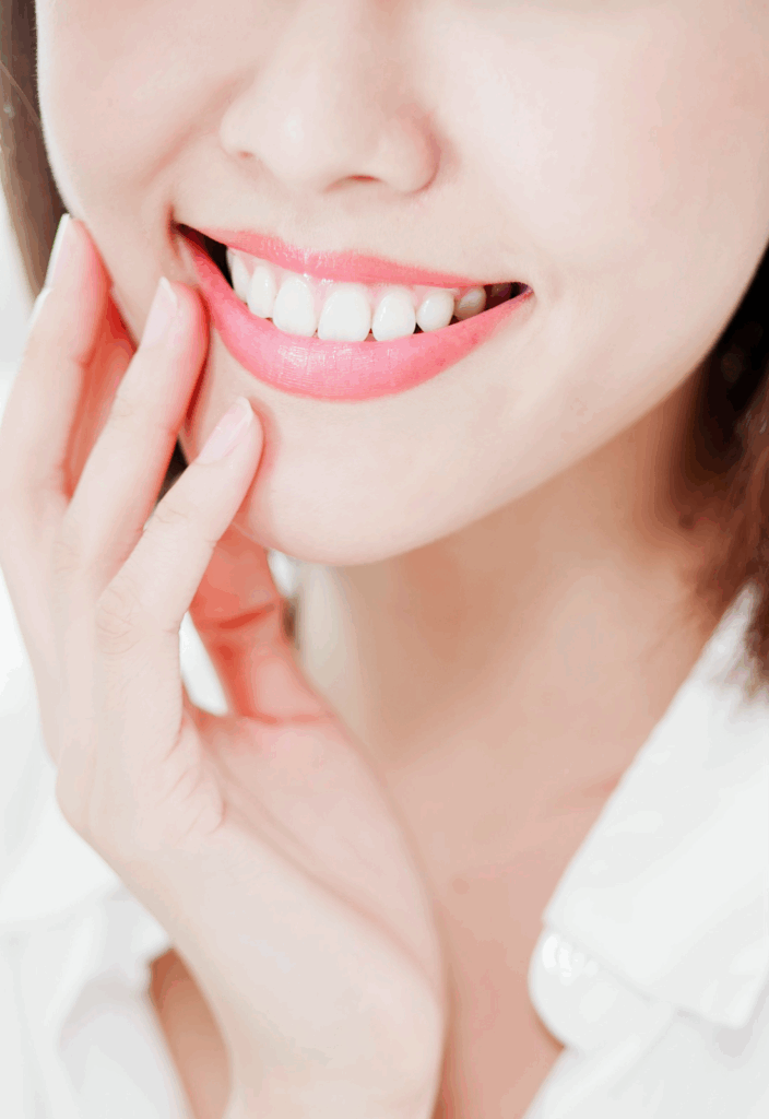 Close-up of a woman smiling with healthy teeth and touching her jaw.