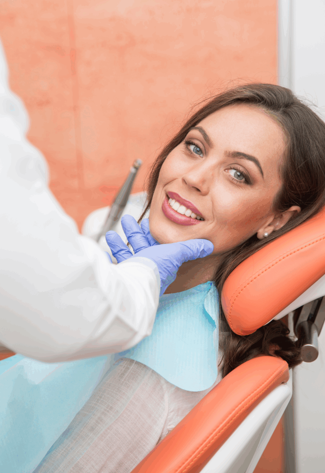 A smiling woman sitting in a dental chair while the dentist holds her jaw.