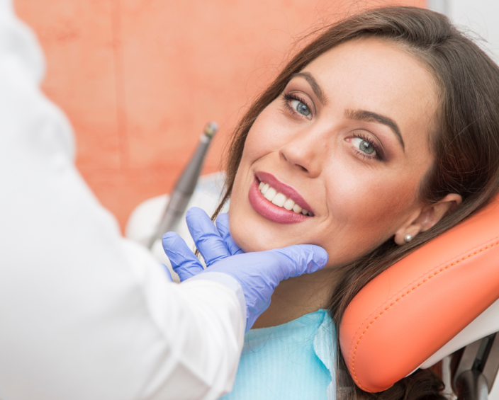 A smiling woman sitting in a dental chair while the dentist holds her jaw.