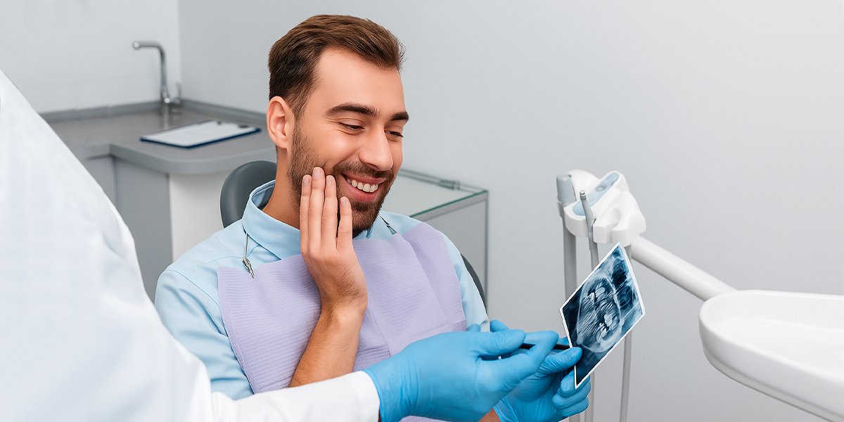 A man sitting in a dental chair looking at an X-ray image of his teeth.