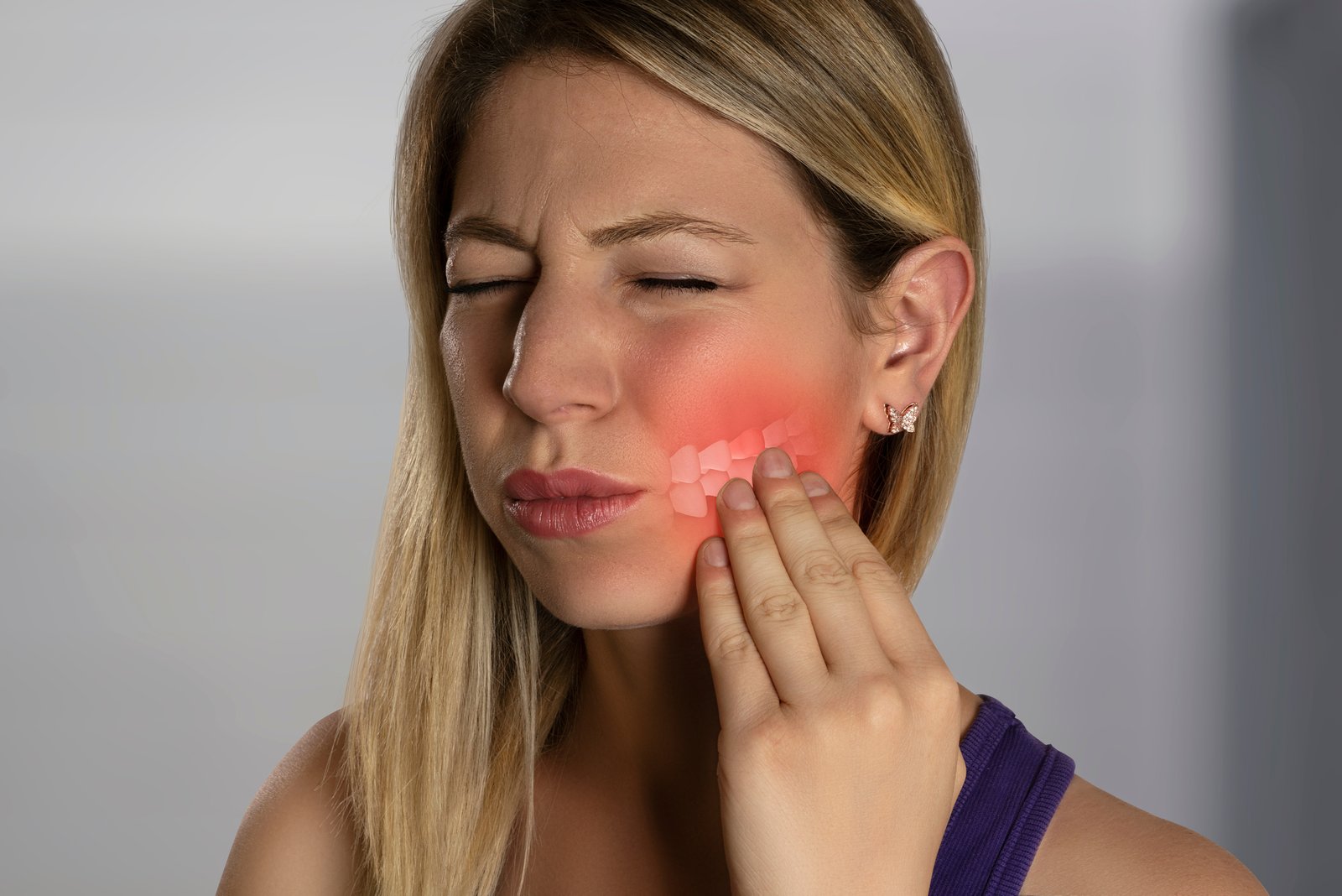 A woman holding her cheek in pain with redness highlighting a toothache.