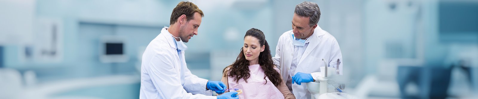 Two dentists show a dental model to a patient during a consultation.