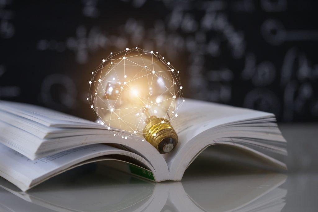 A light bulb resting on an open book with a glowing network design around it.