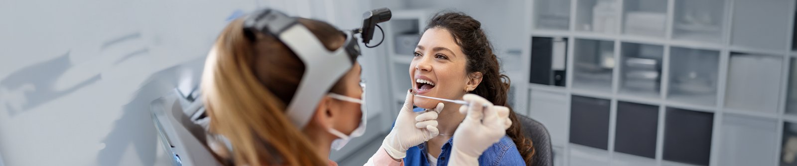 A dental professional examines a patient’s mouth with a dental mirror during a checkup.
