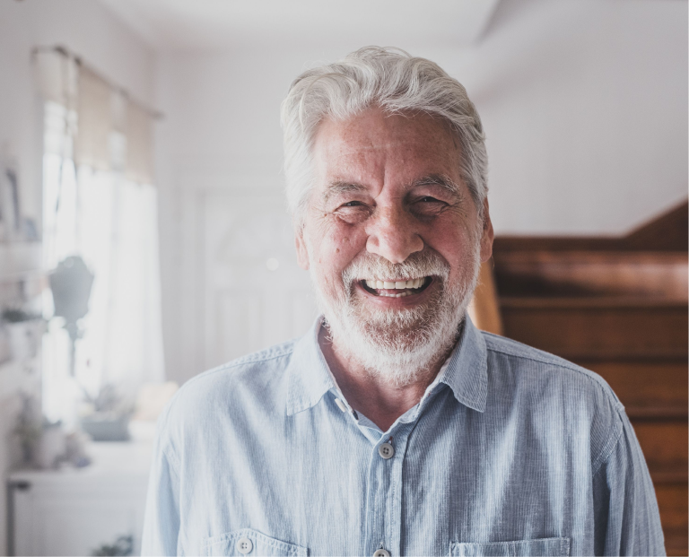 A smiling older man with healthy teeth standing indoors.
