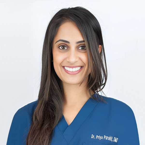 Dr. Priya Meghpara, FAGD wearing blue dental scrubs smiling against a light background.